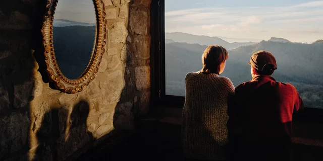 Two white individuals looking out of a window to an impressive view of nature