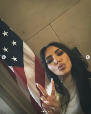 Second Image of Kim Kardashian's Post (No.2), depicted infront of U.S. flag, making the peace sign with her hand and duck face with her lips